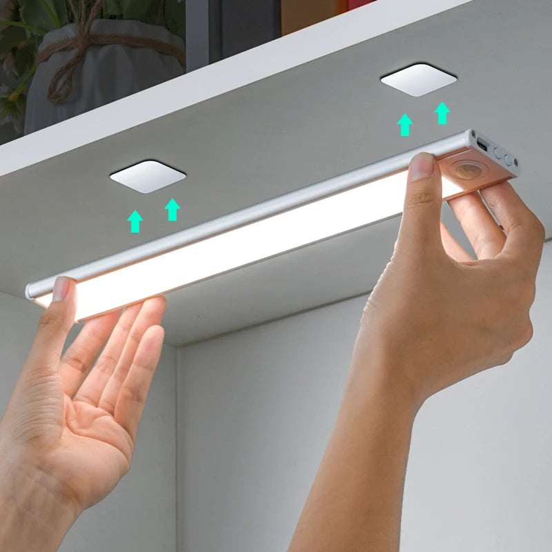 Person installing a LED strip light under a cabinet with a smartphone app control.